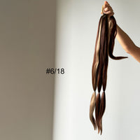 Hair extensions held by a hand with a neutral background