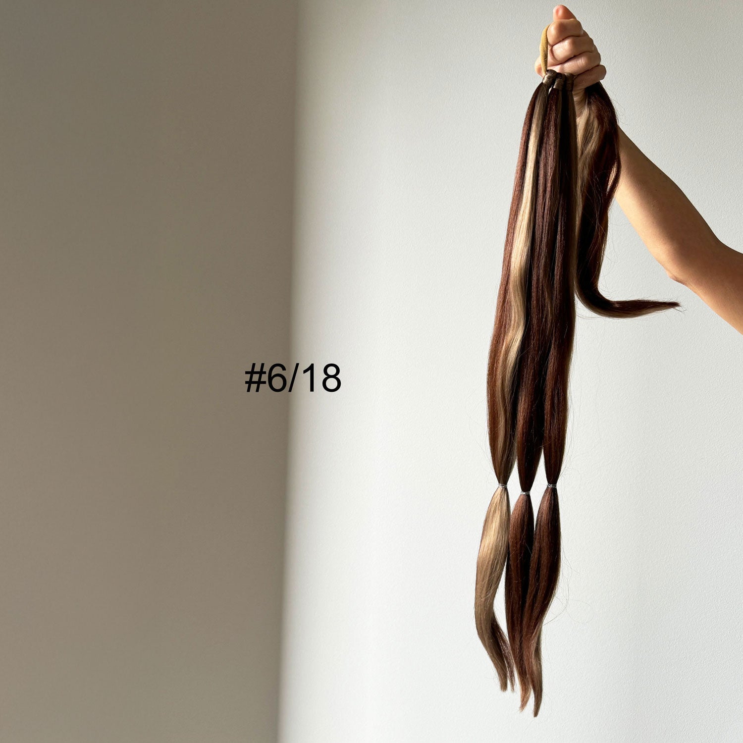 Hair extensions held by a hand with a neutral background