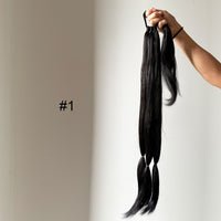 Black hair extensions held by a hand against a plain background