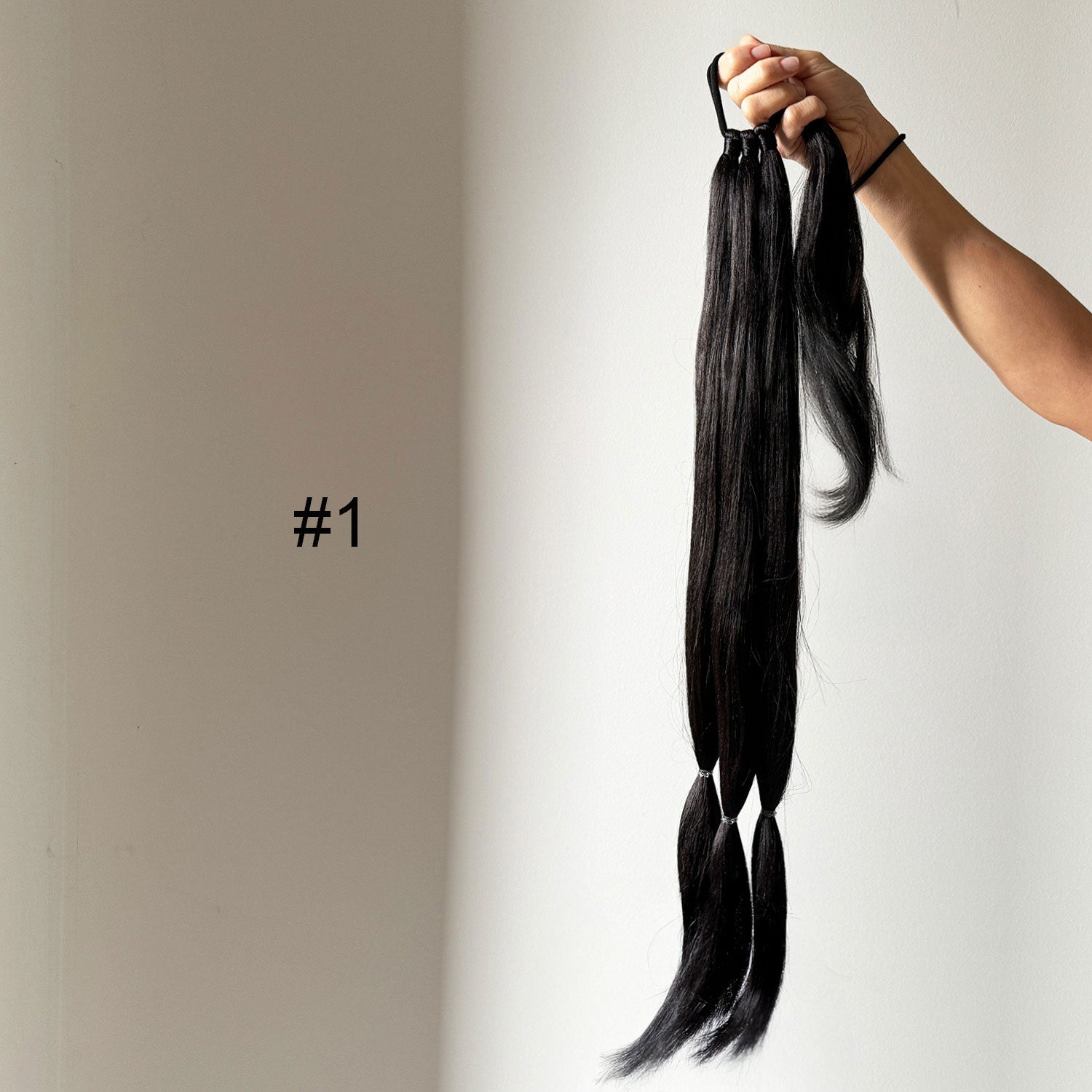 Black hair extensions held by a hand against a plain background