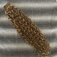Curly hair extension on a textured fabric background, shade is Dirty Blonde