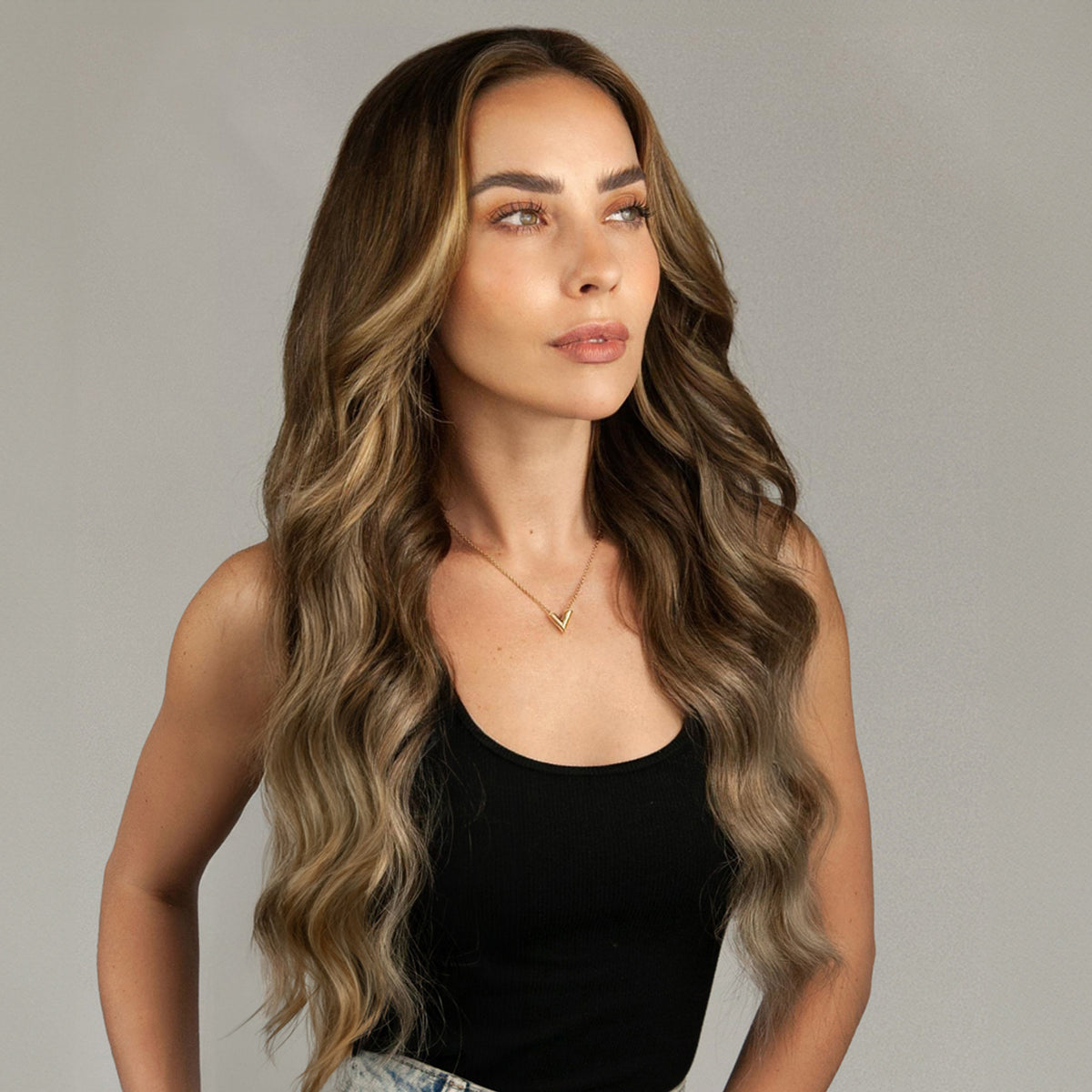 Woman with long, wavy hair extensions wearing a black top against a plain background