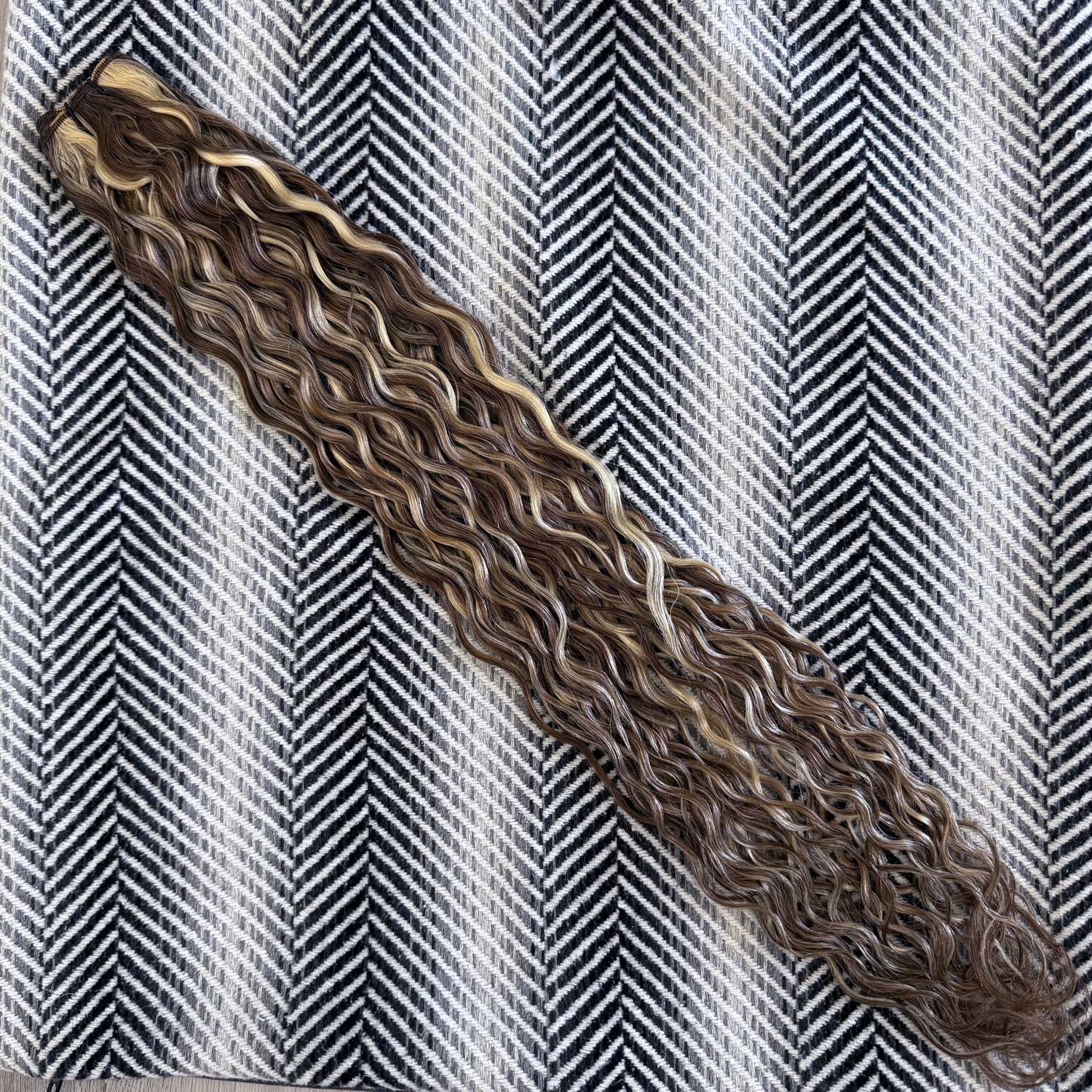 Curly human hair extensions on a striped fabric background