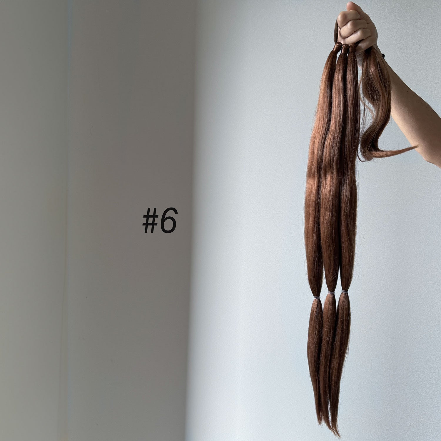 Brown hair extensions held by a hand against a plain background