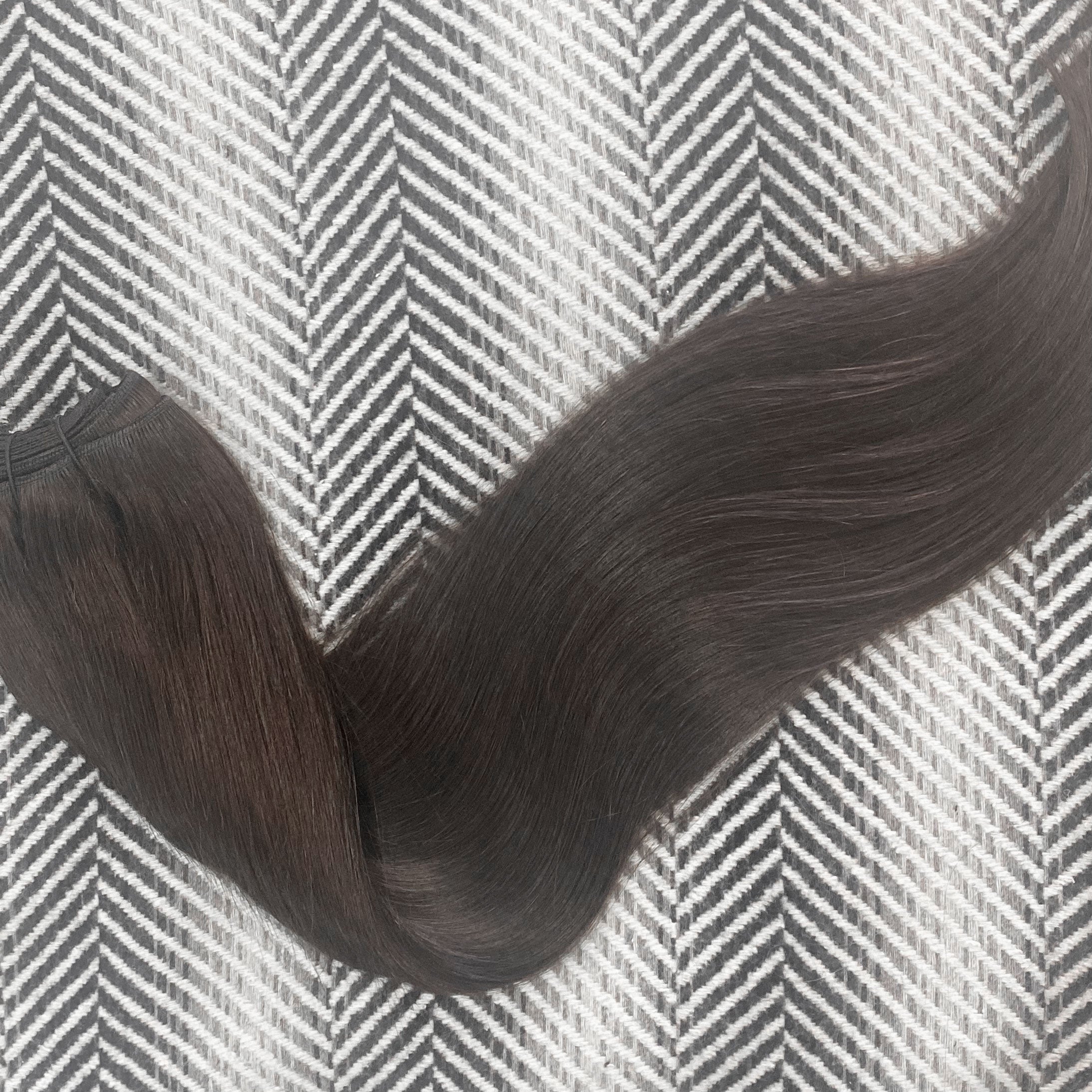 Dark brown hair extensions on a textured gray and white background