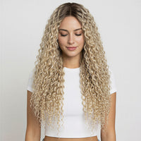 Woman with long, wavy blonde curly hair extensions wearing a white top against a plain background