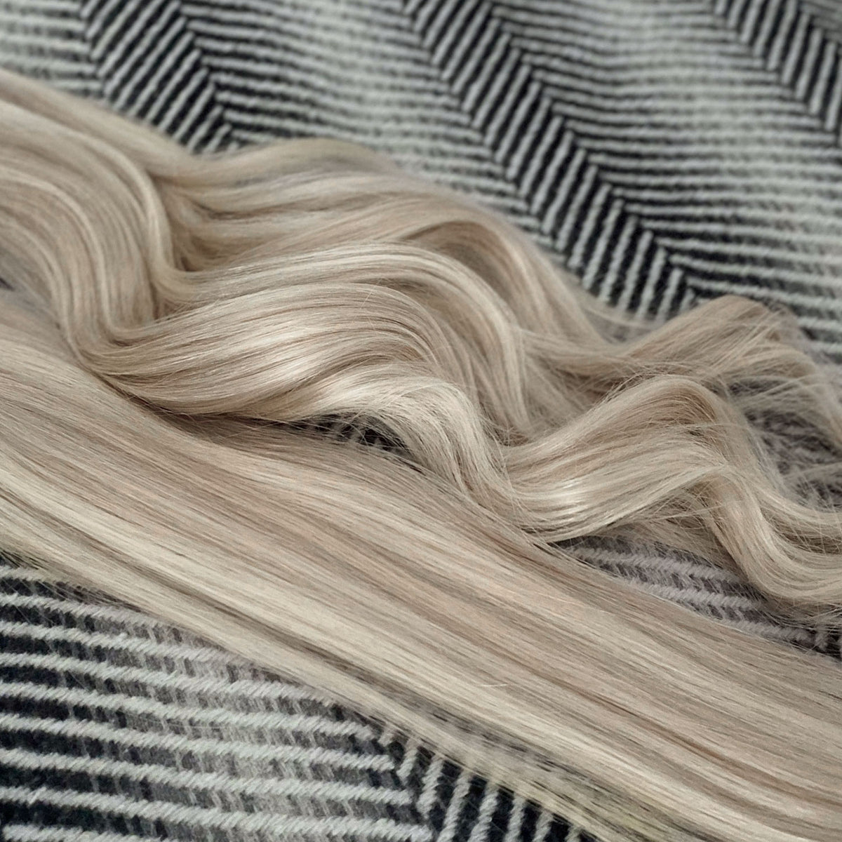 Long, wavy blonde hair extensions or a wig laid out on a black and white herringbone patterned fabric background.