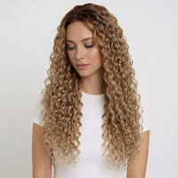 Woman with long, wavy naturl blonde curly hair extensions wearing a white top on a light background