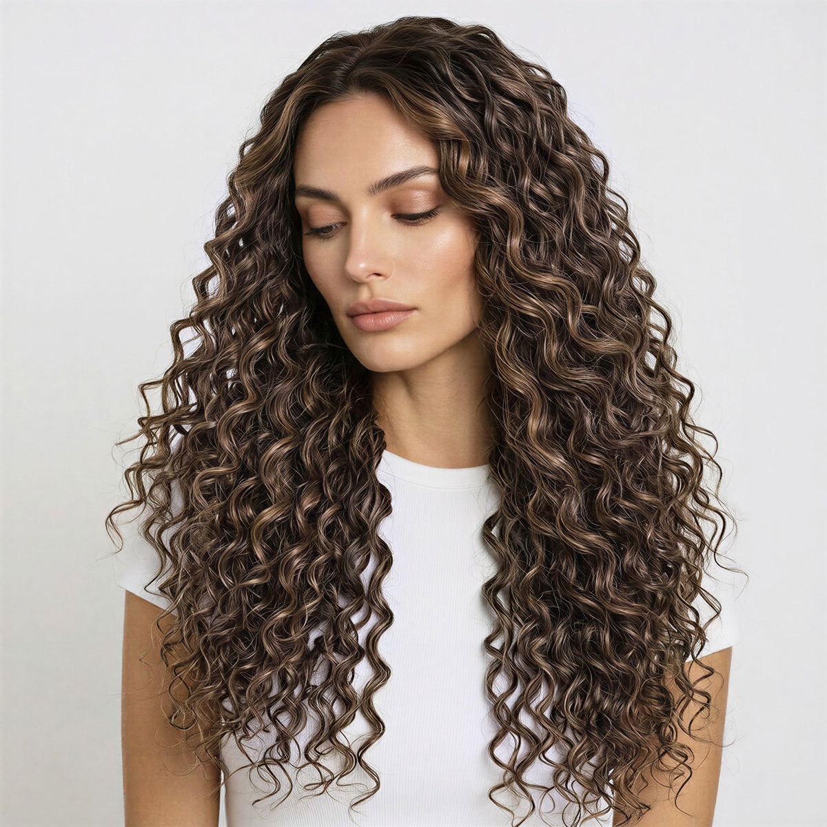 Woman with long, wavy ash and dark brown curly hair extensions wearing a white top on a light gray background
