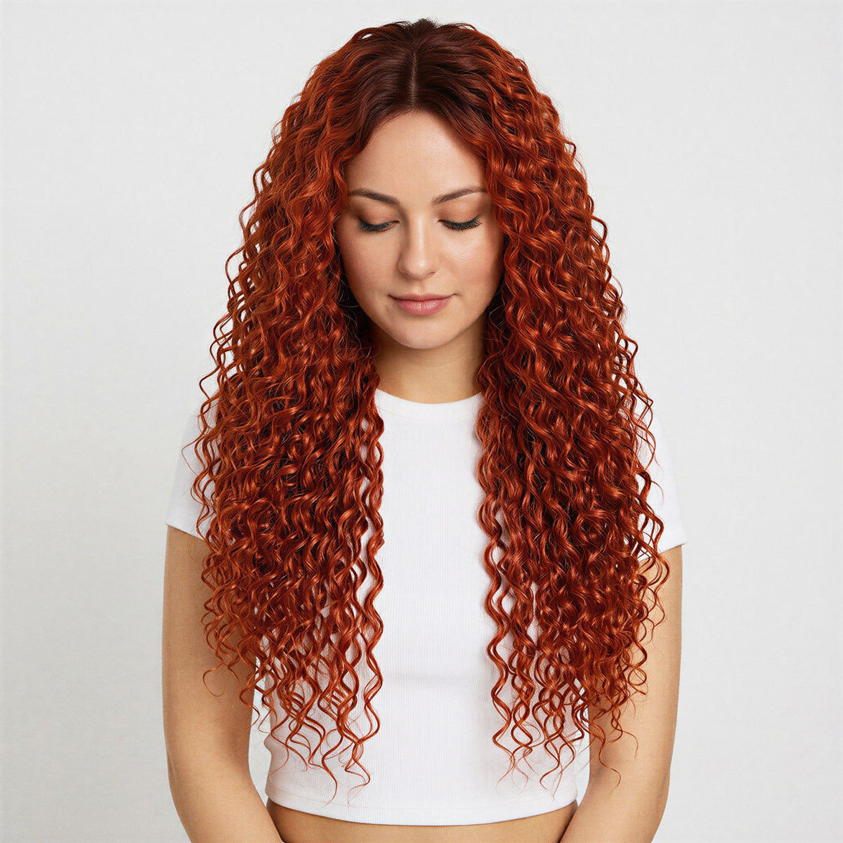 Woman with long, wavy red copper curly hair extensions wearing a white top on a light gray background