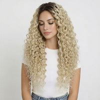 Woman with long, curly clip in hair extensions blonde wearing a white top and blue jeans on a light gray background