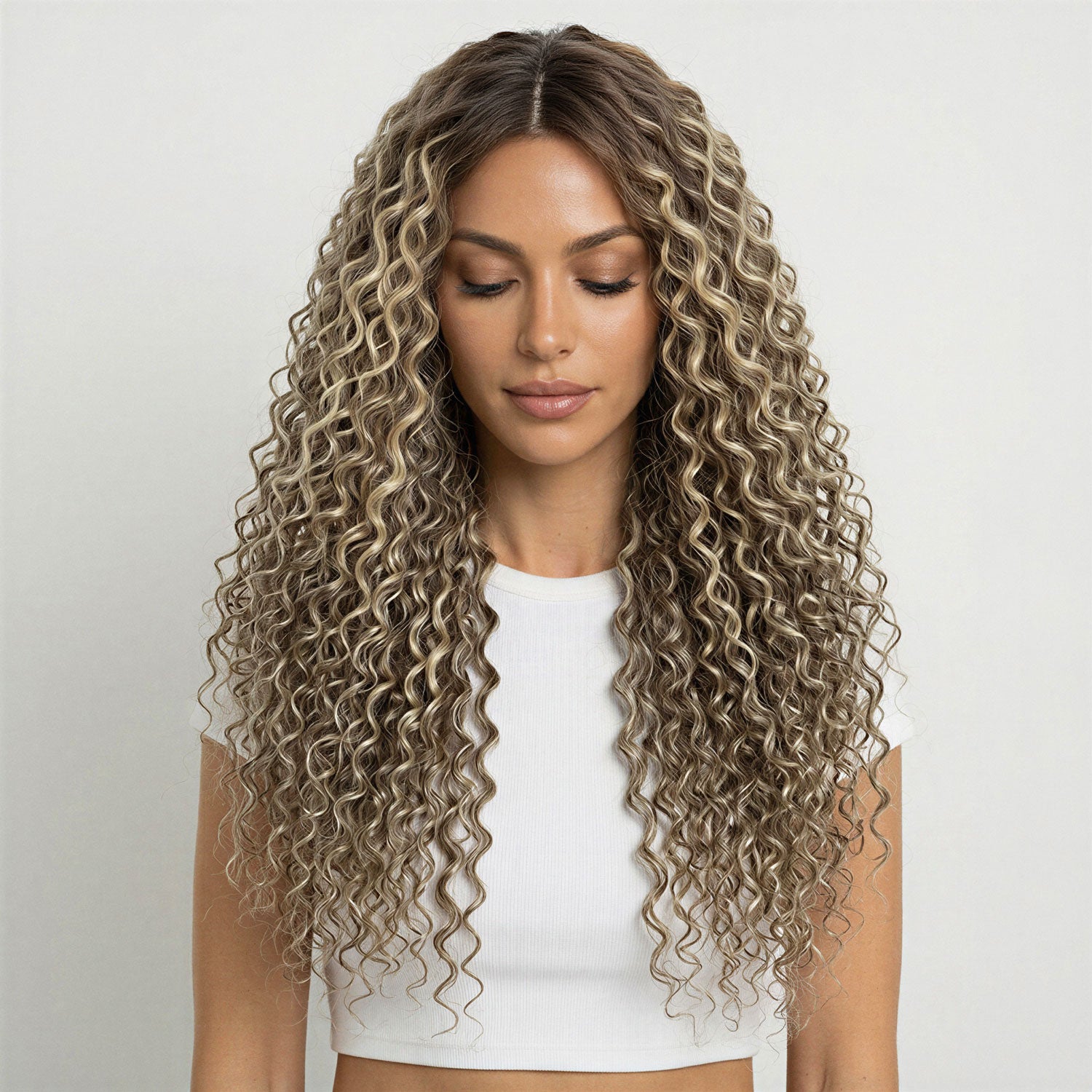 Woman with long, wavy ash brown  and platinum blonde mix curly hair extensions wearing a white top on a light grey background