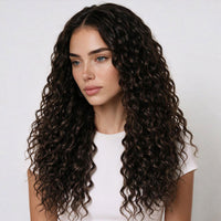 A woman with long, dark brown clip in curly hair extensions, tightly curled hair wearing a white ribbed t-shirt, photographed against a clean, light gray studio background.