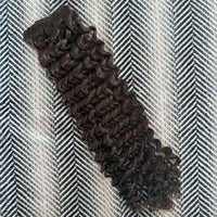 Brown curly hair extensions on a herringbone patterned surface