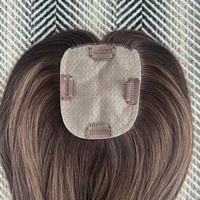 Hair topper with brown hair extensions on a textured surface