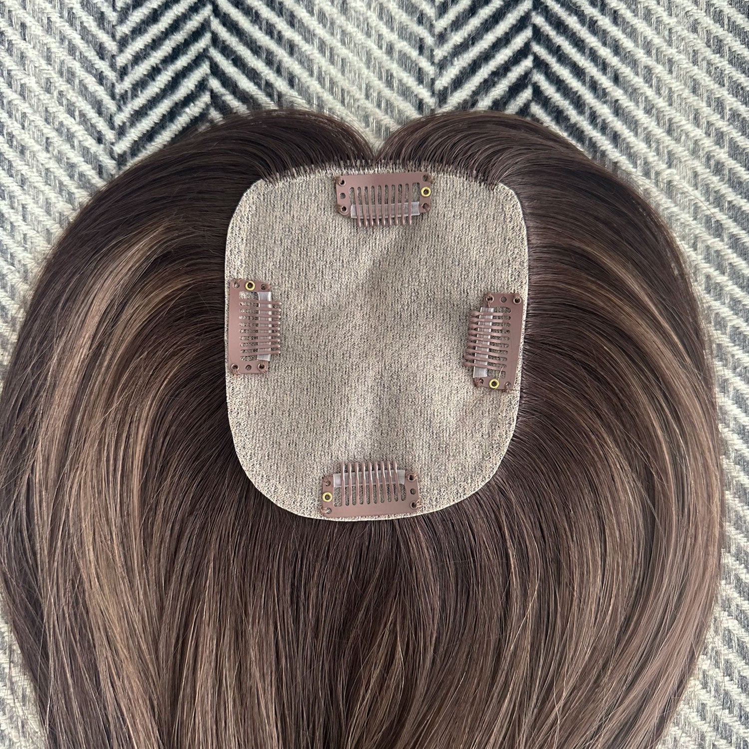 Hair topper with brown hair extensions on a textured surface
