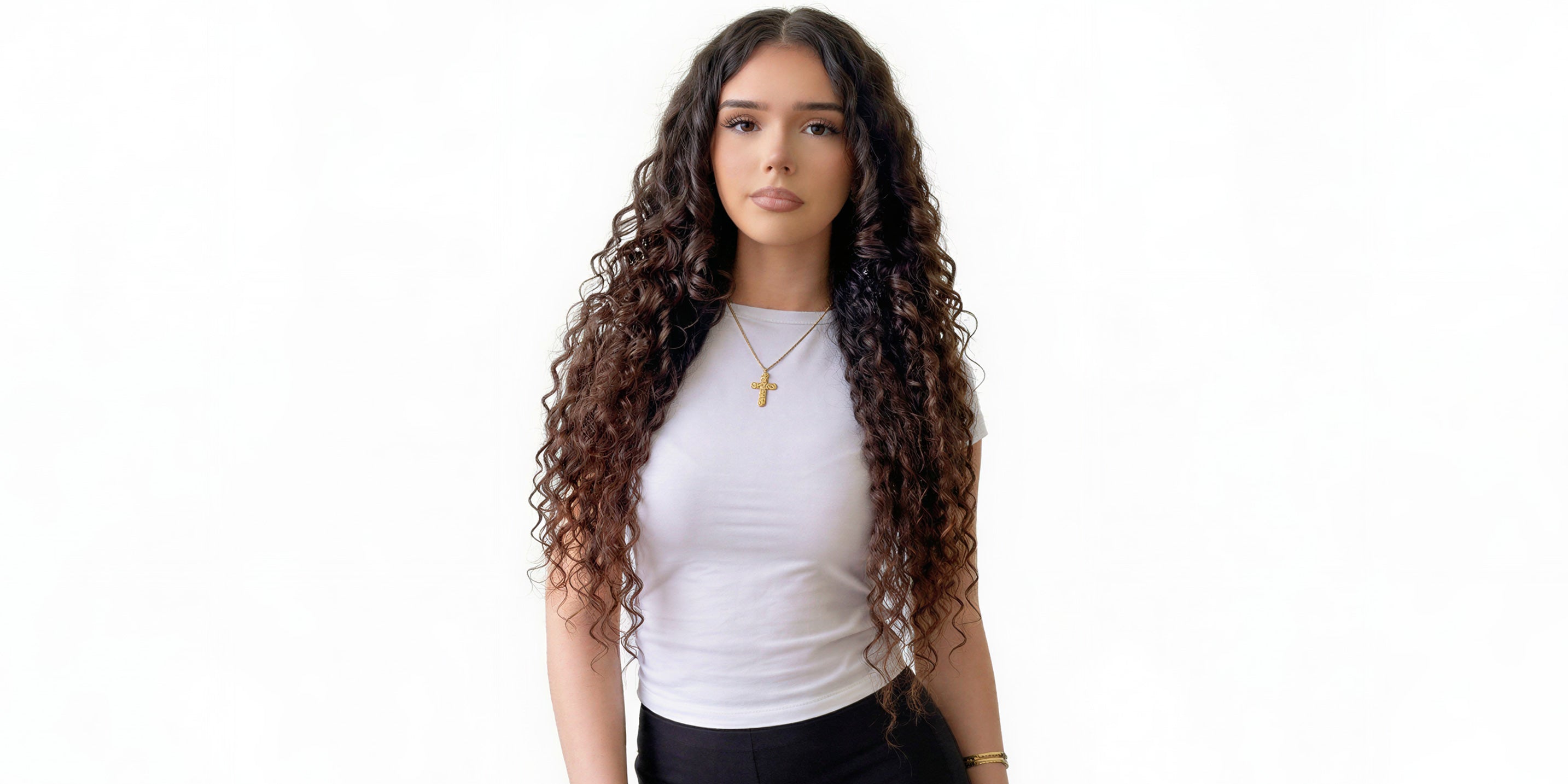 Woman with long, curly hair extensions wearing a white shirt and black pants on a white background