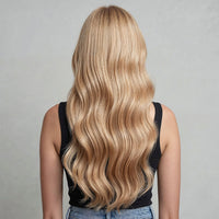 Person with long, wavy honey blonde hair extensions on a gray background