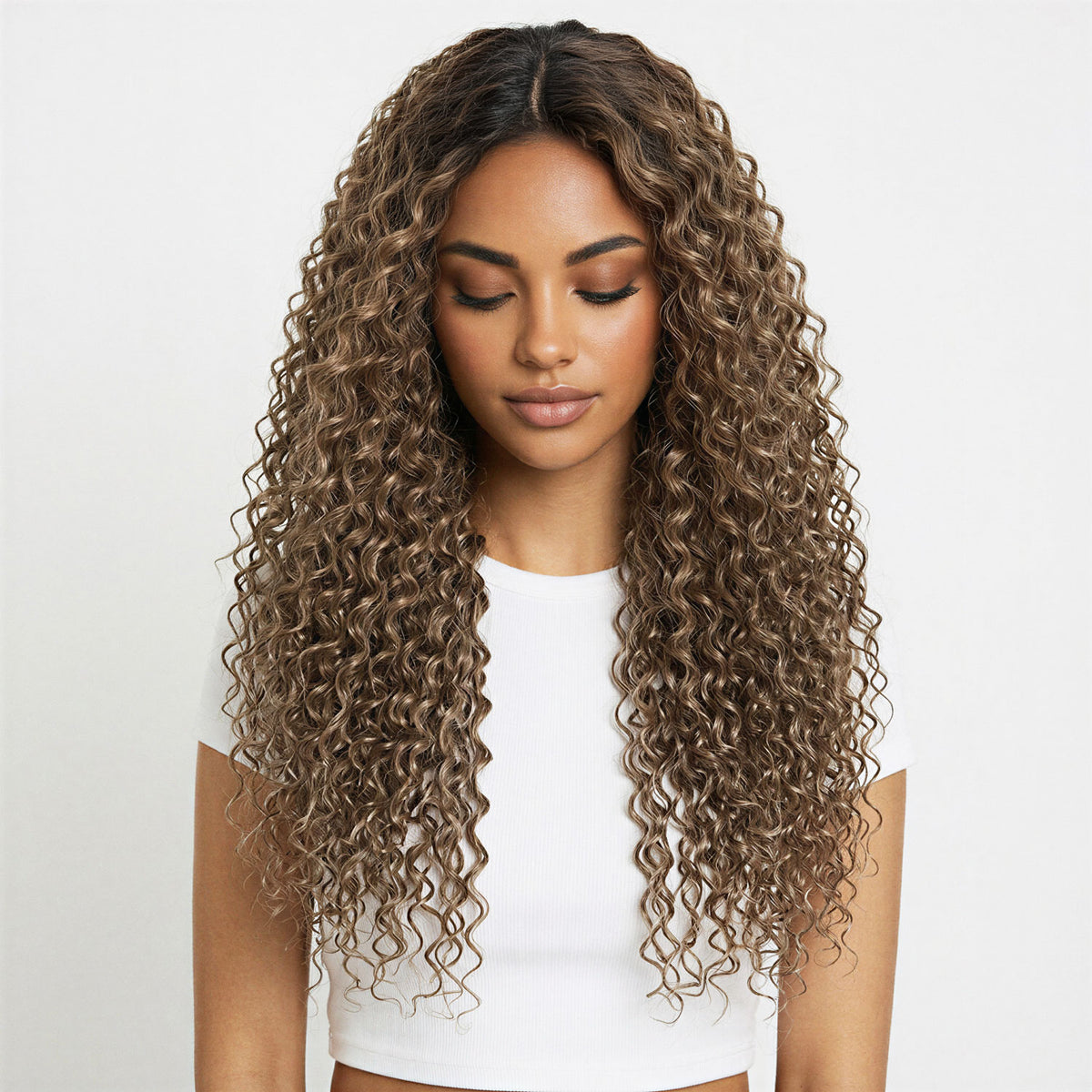 Woman with long, wavy ash brown curly hair extensions wearing a white top on a light grey background