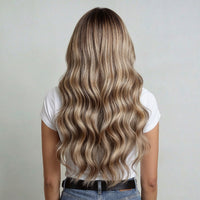 Person with long, wavy, blonde hair extensions wearing a white shirt and jeans on a plain background