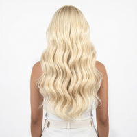 Person with long, wavy vanilla blonde hair extensions on a white background