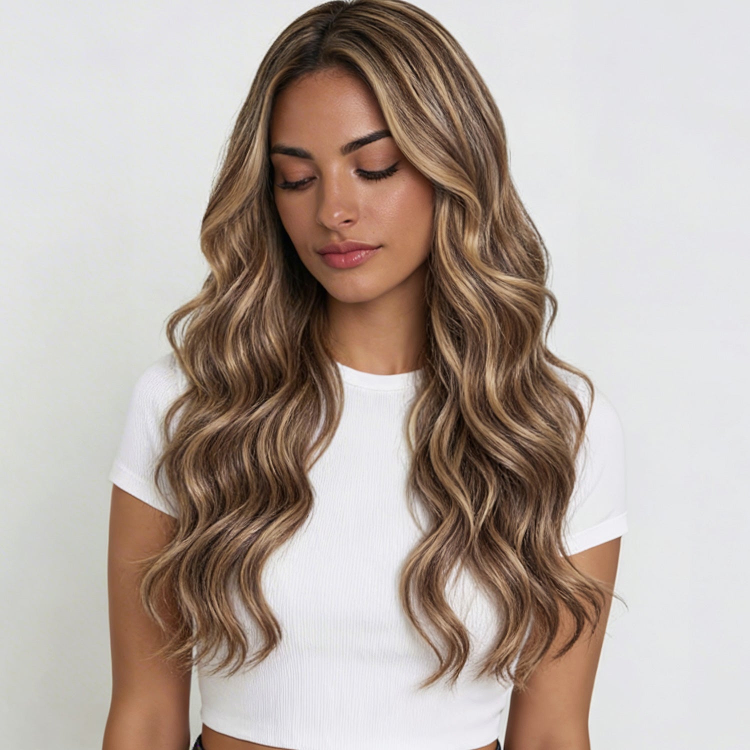 Woman with long, wavy, blonde hair wearing a white top on a light background