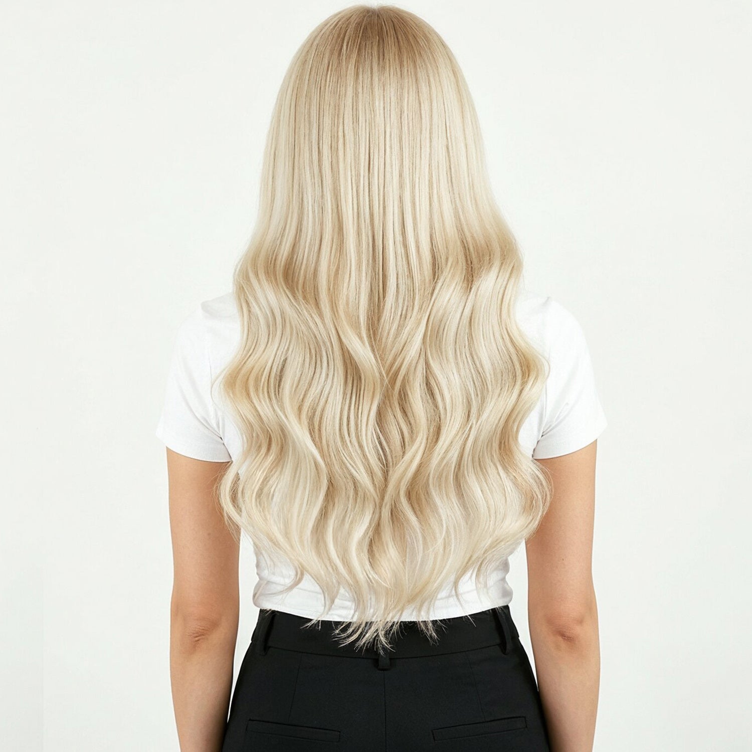 Person with long blonde hair extensions wearing a white shirt and black pants on a white background