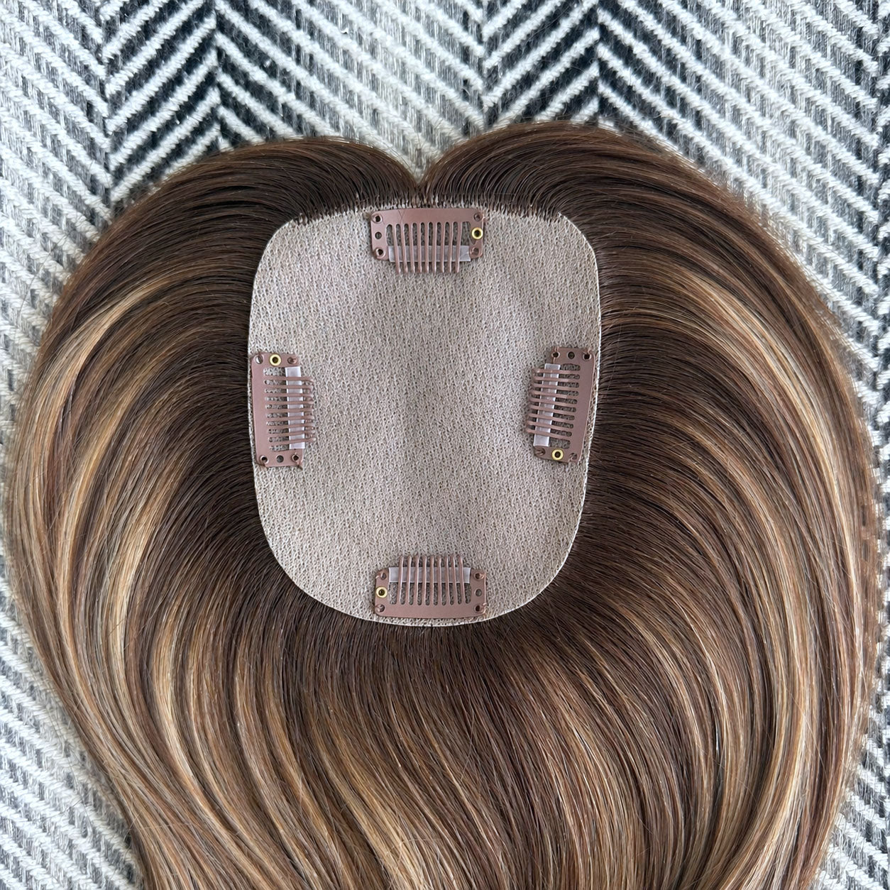 Brown hair extension with a gray adhesive patch on a textured surface
